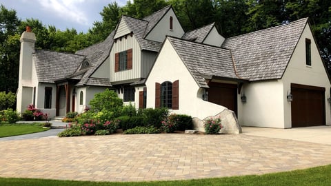 large brick drivway leading to garage with flower beds