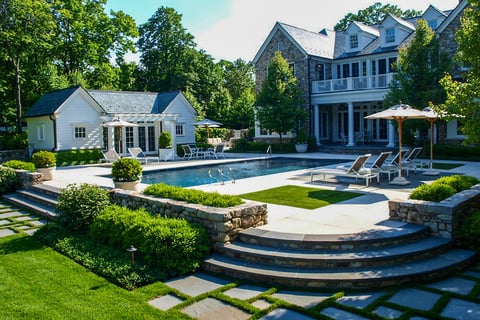 Residential backyard with a large private pool surrounded by stone pathways and bushes