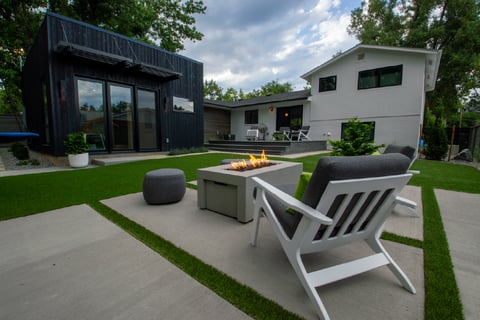 Residential backyard with stone firepit and view leading to the back of a black house and white house