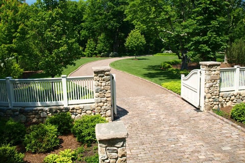 Residential cobblestone driveway featuring a white pickett fence with stone pillars