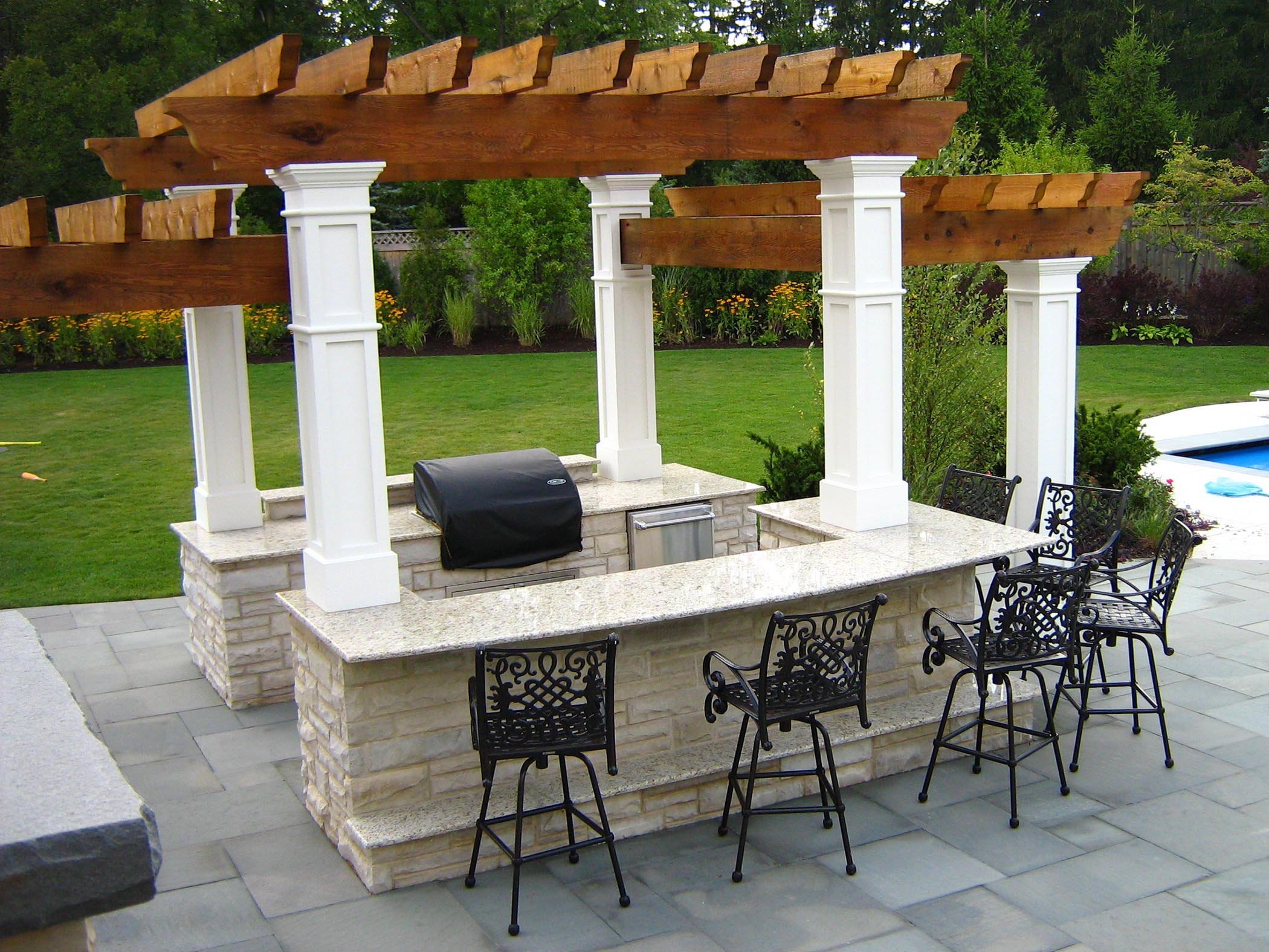 backyard pergola outdoor kitchen with paver patio next to pool