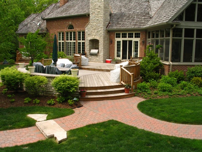 circular wooden deck with stone fireplace and paver pathways in backyard 