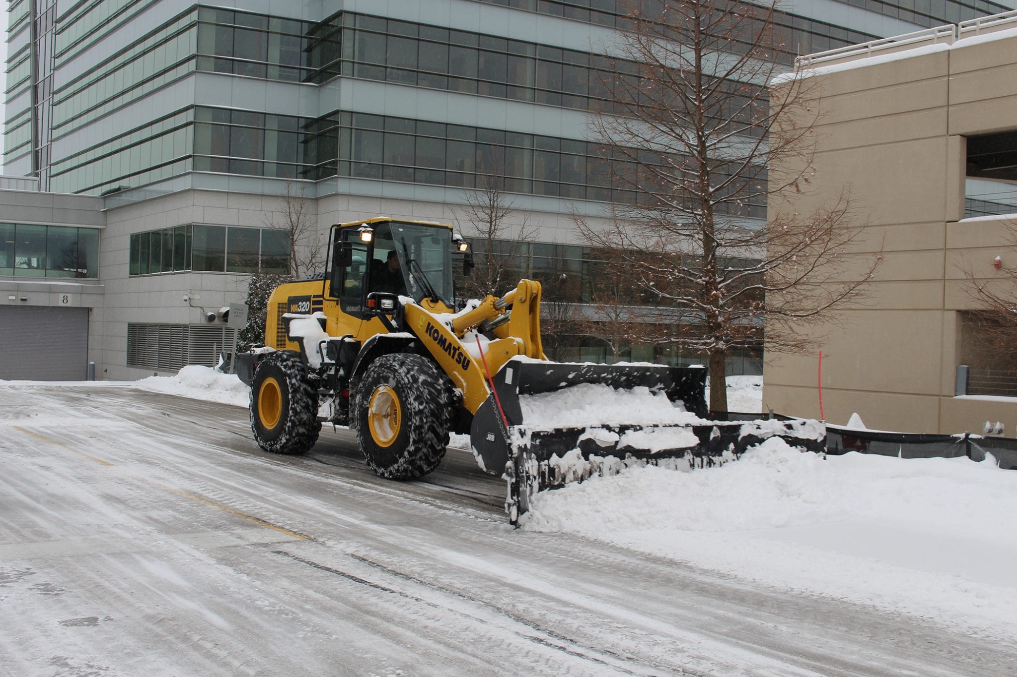 plow clearing snow in parking lot near business