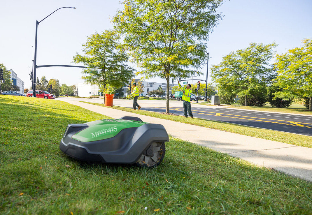 robotic mower with logo and crew in background