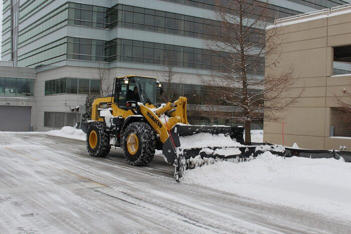 Bulldozer plowing snow in commercial parking lot 