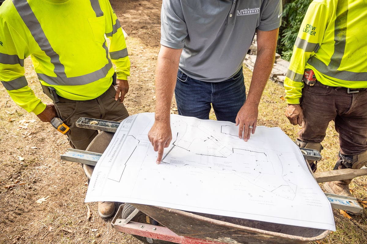 crew pointing at a landscape design blueprint in homeowner backyard