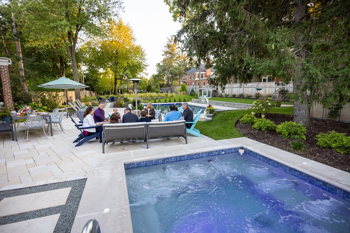 Residential landscape design family sitting by fire on patio near spa